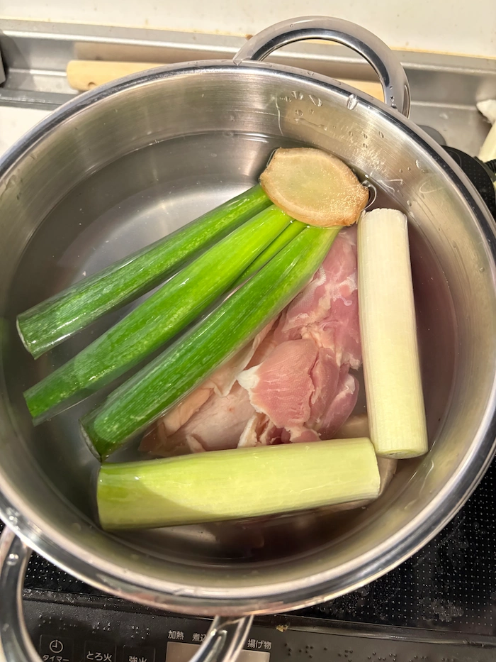 鍋に材料のネギ、生姜、鶏肉、水を入れ似ている写真